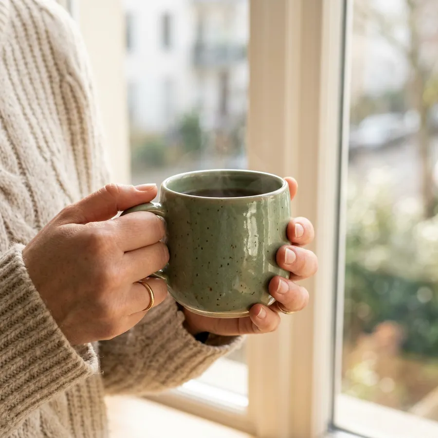 La misma taza en las manos de alguien junto a una ventana